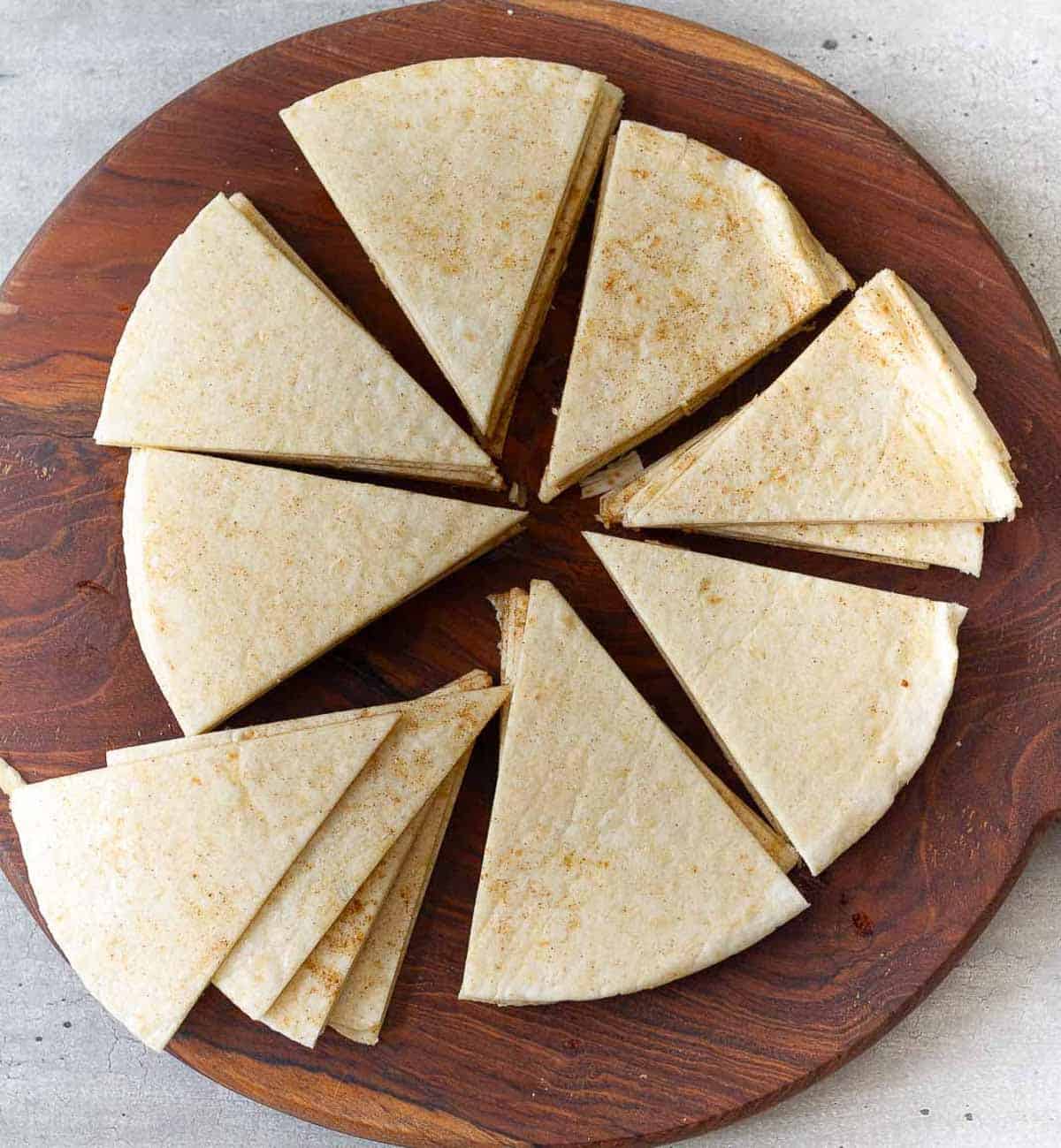 Seasoned tortillas cut into triangles on a wooden board.