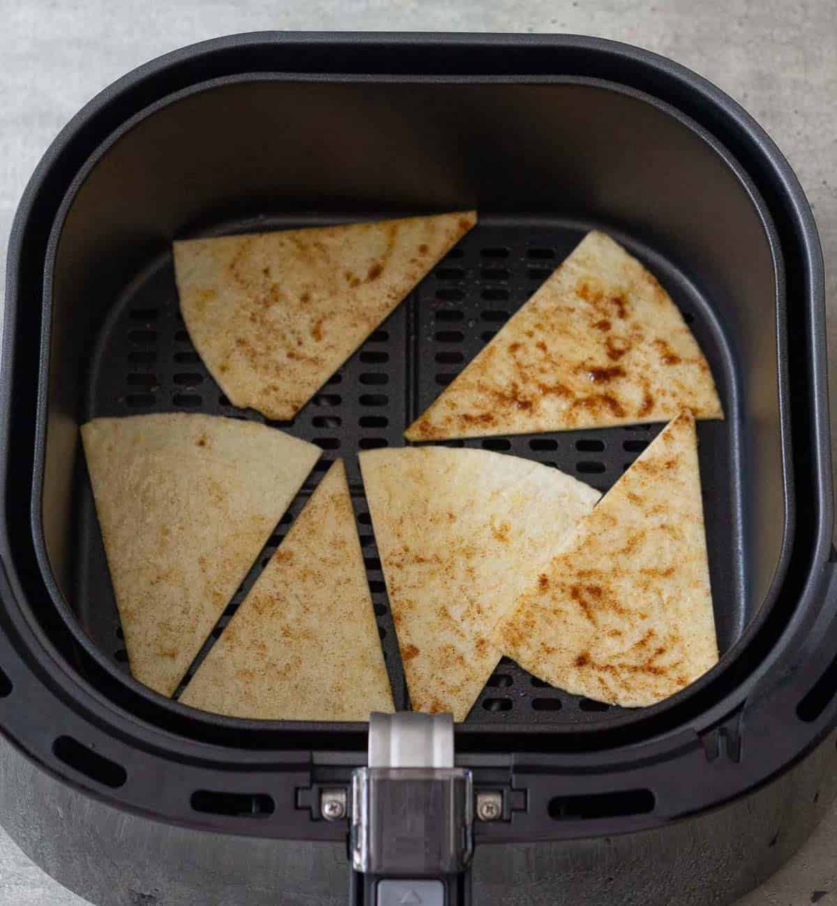 Seasoned tortilla triangles in a single layer in the air fryer basket.