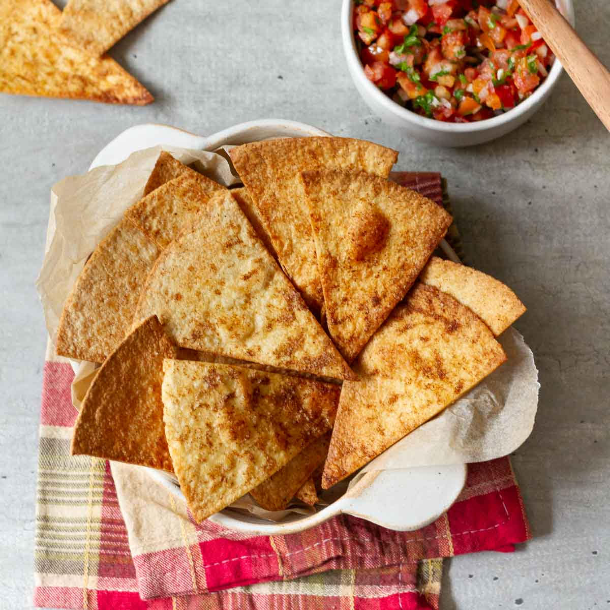 Air fryer tortilla chips in a paper lined bowl with salsa in the background.