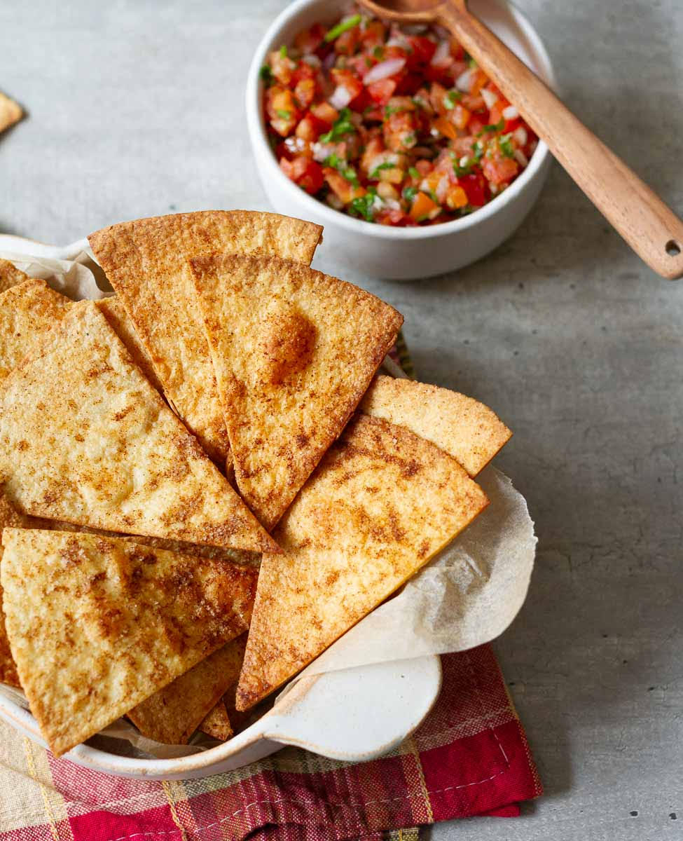 air fryer tortilla chips in a serving dish with tomato salsa.