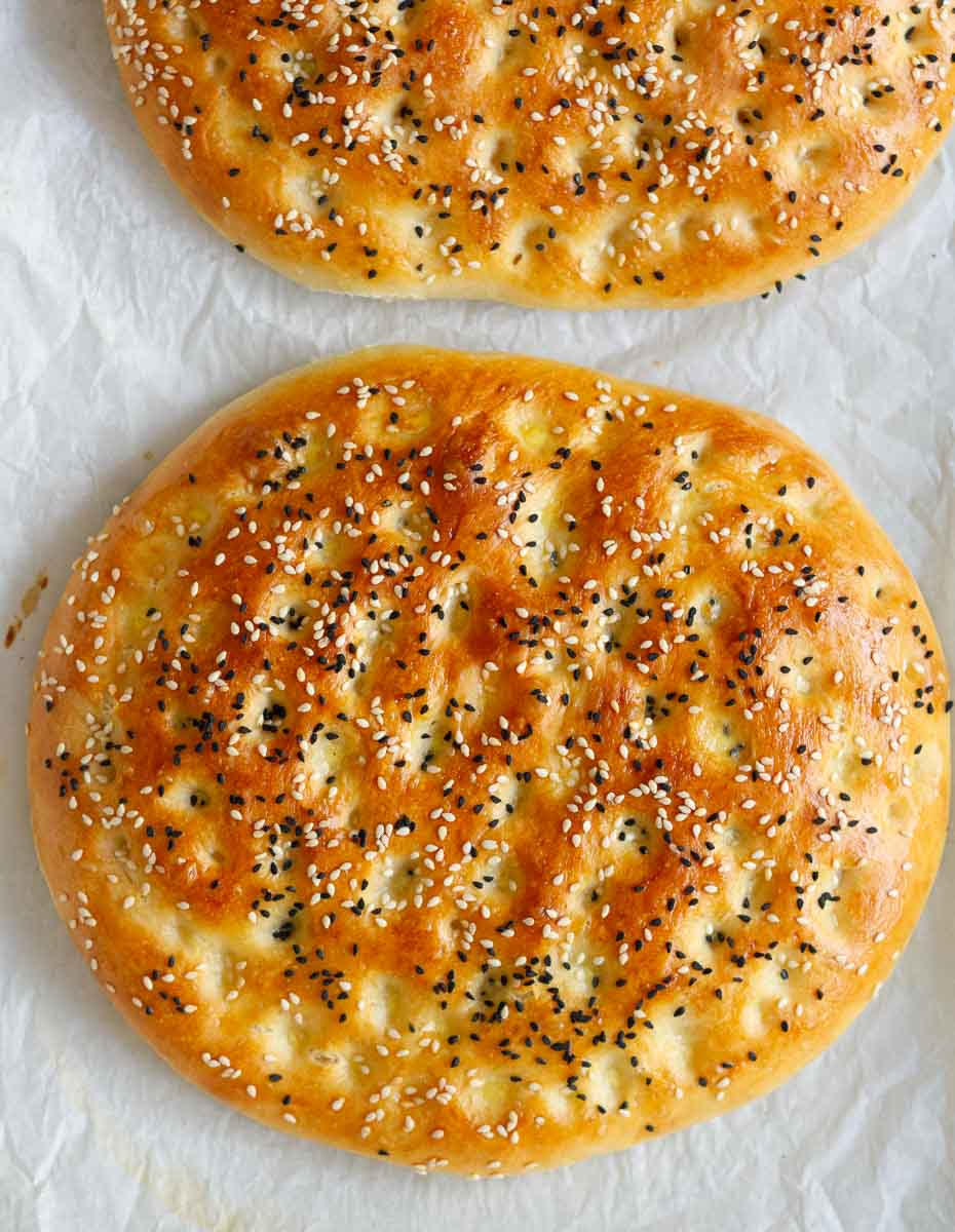 2 loaves of flatbread with seeds on top on parchment paper.