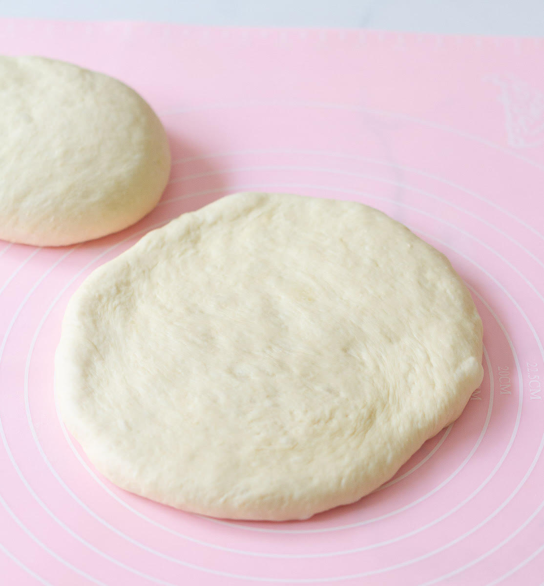 Bread dough shaped into a circle on a pink silicone mat.