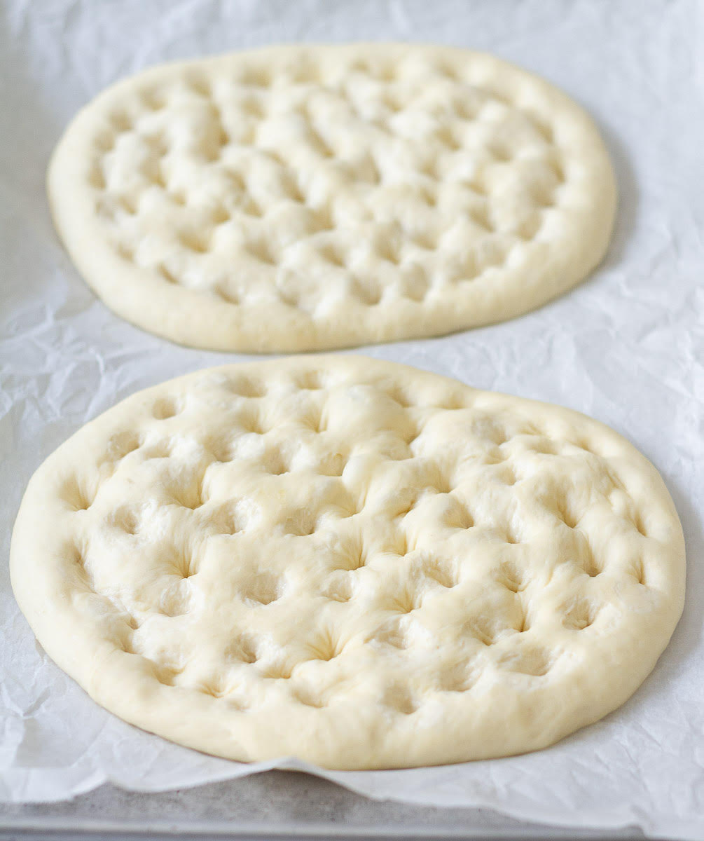 Dough circles with indents on parchment paper.