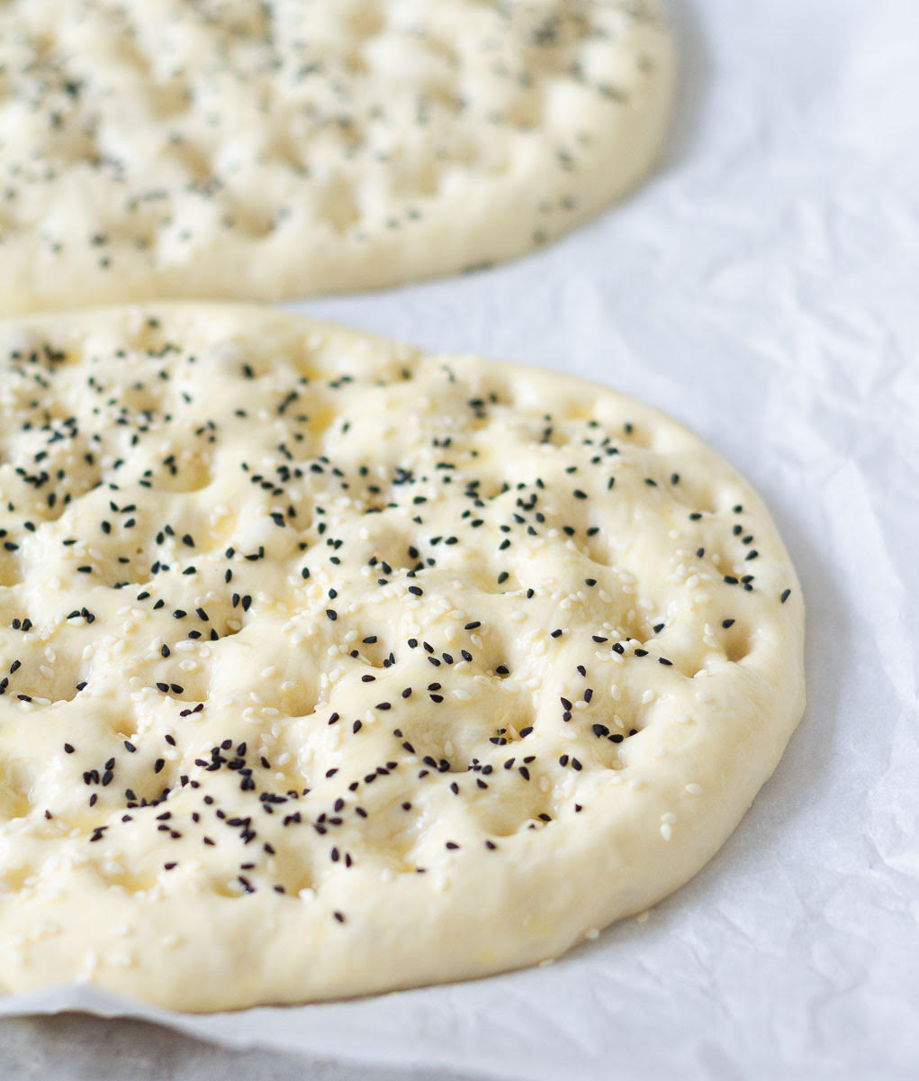 Dough circles sprinkled with sesame and nigella seeds on a white parchment paper.
