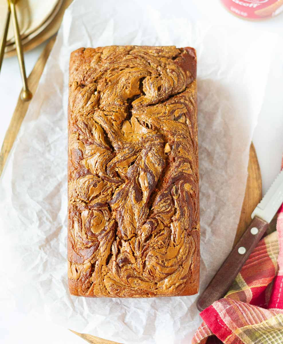 A loaf of biscoff banana bread with a knife on white paper.