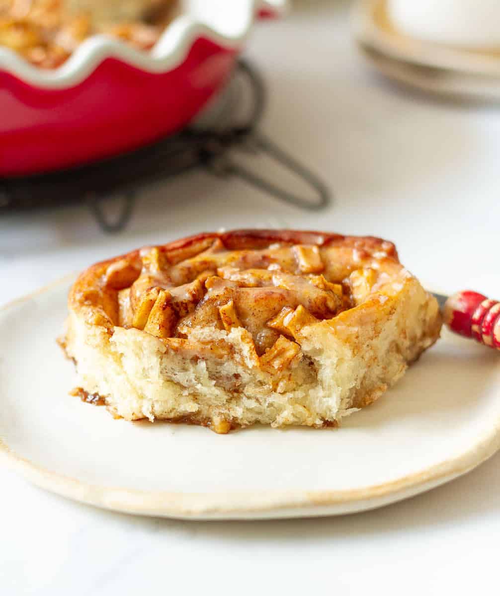 Apple pie cinnamon roll on a small plate with a red fork.
