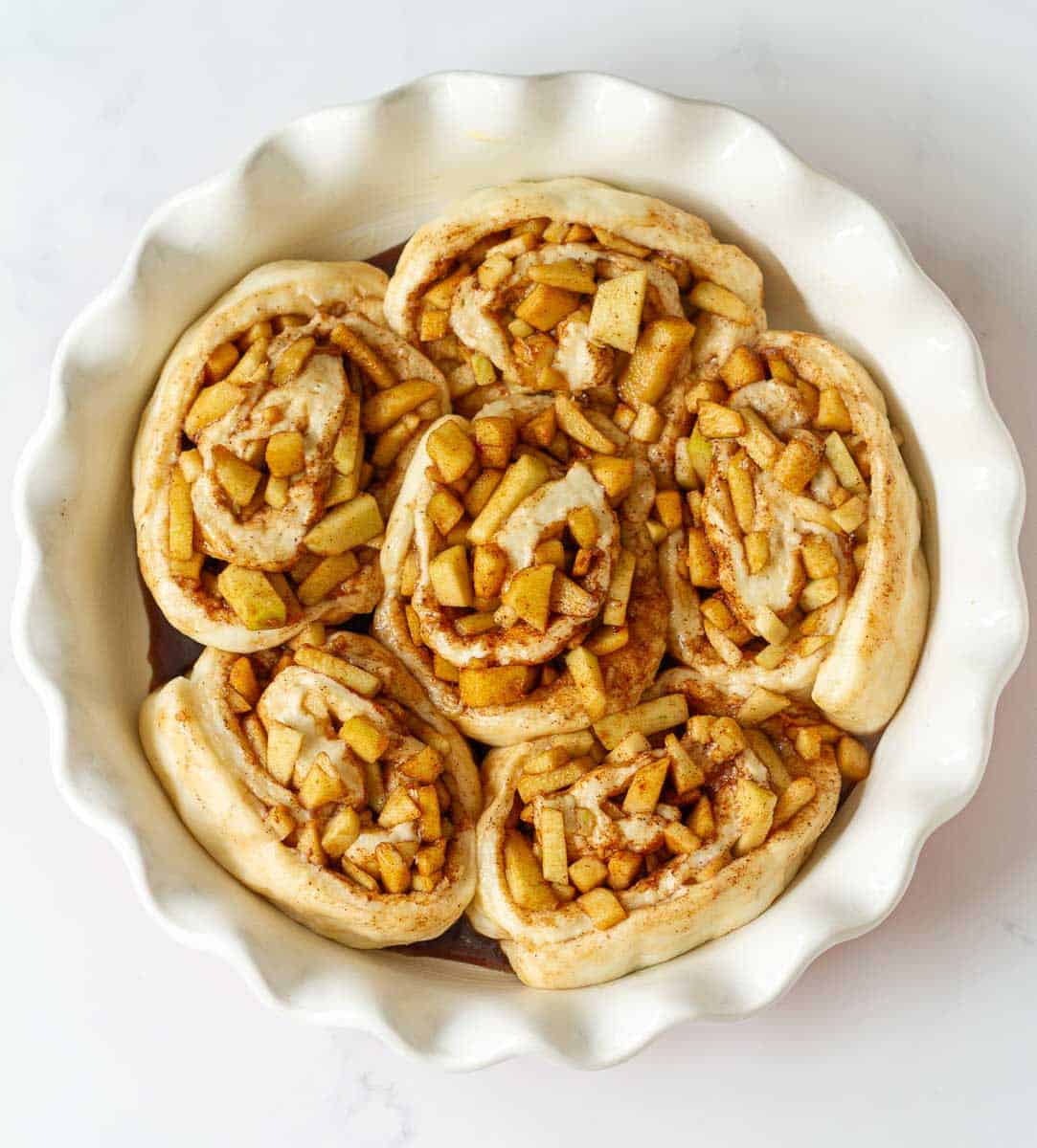 Proofed apple rolls in a round baking pan.