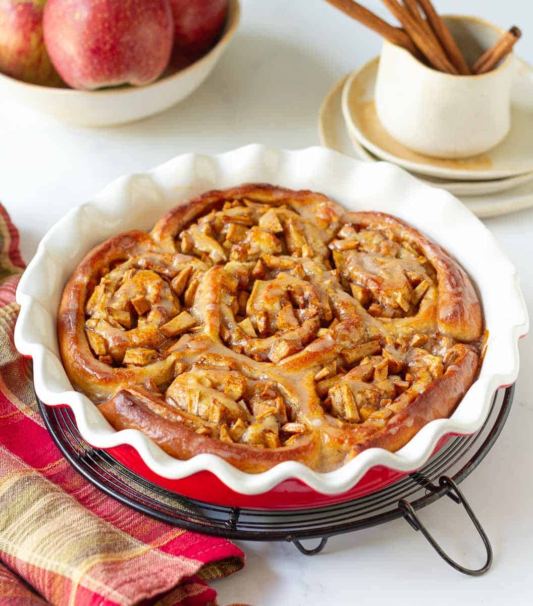 Apple Pie Cinnamon Rolls with cinnamon glaze in a round baking dish.