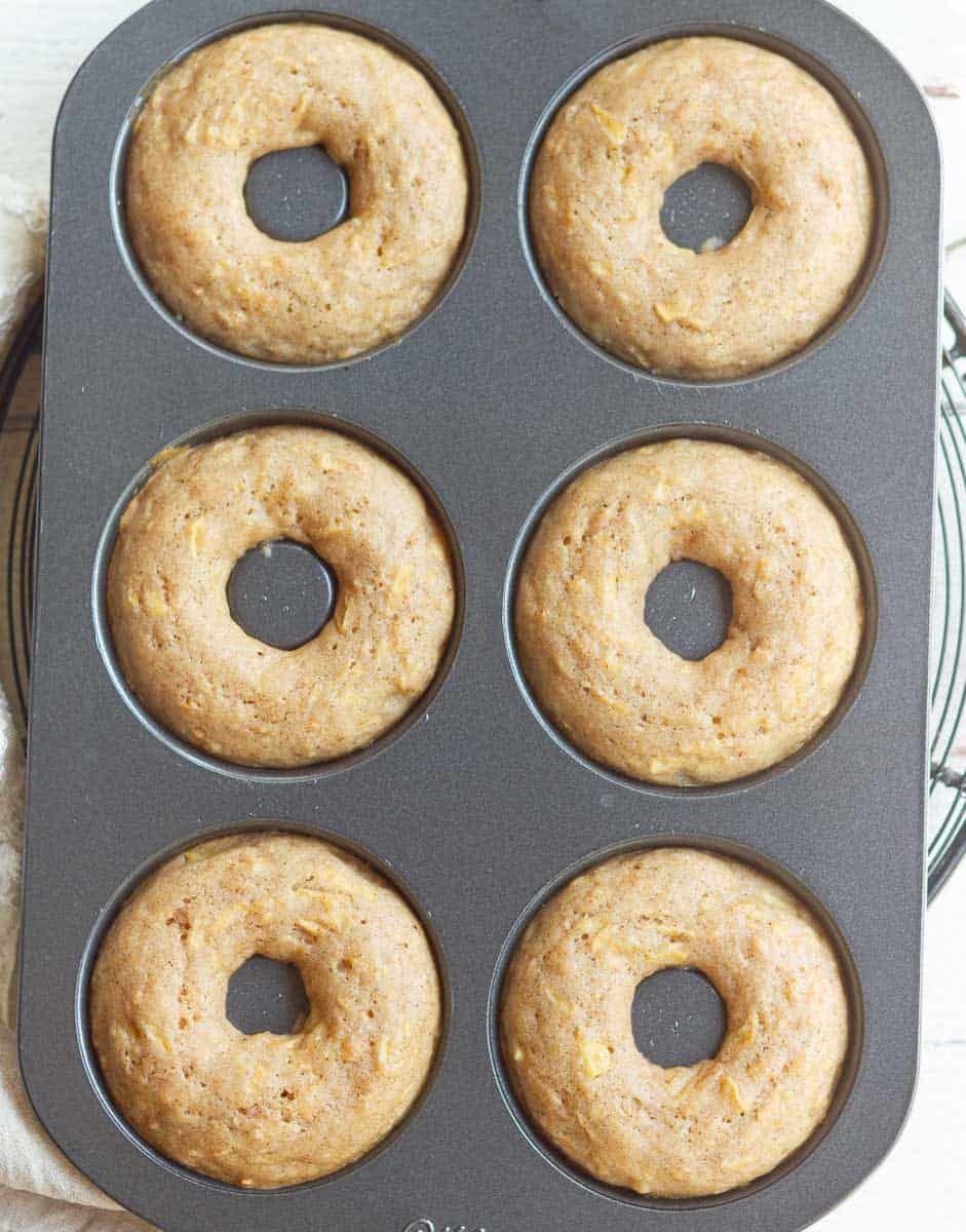 Baked apple donuts in a metal donut pan.