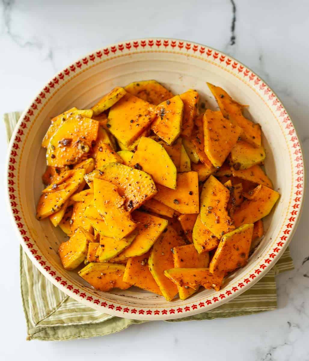 Sliced butternut squash seasoned with olive oil and spices in a bowl.