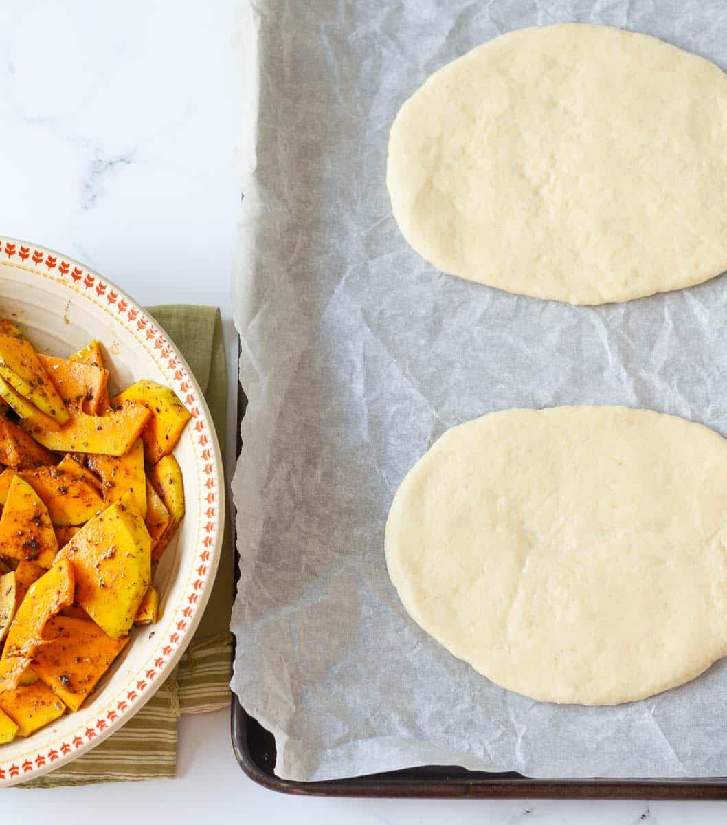 Rolled out dough on a tray and seasoned squash in a bowl.
