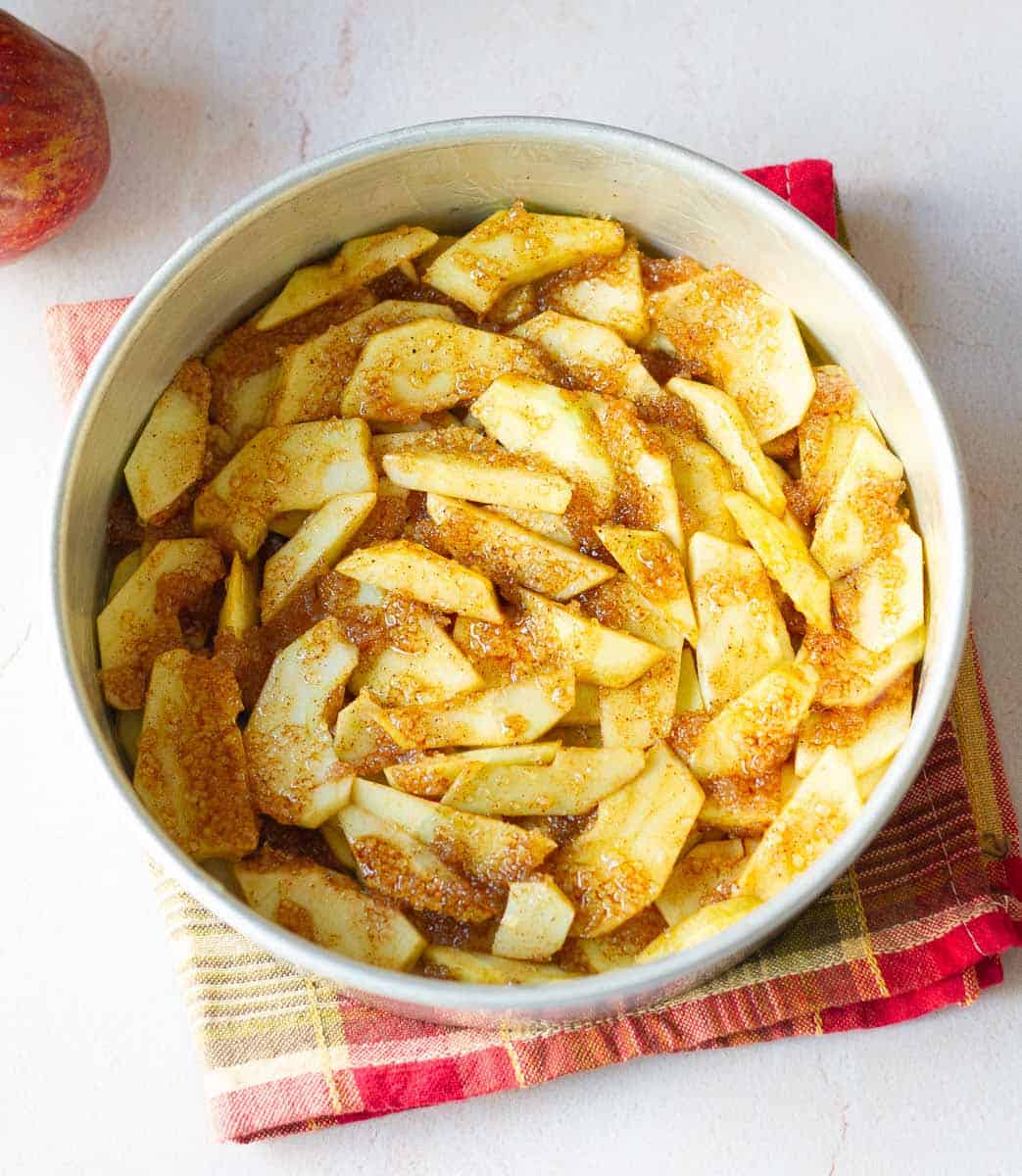 Apples in the cake tin with a mixture of butter, cinnamon powder and sugar.