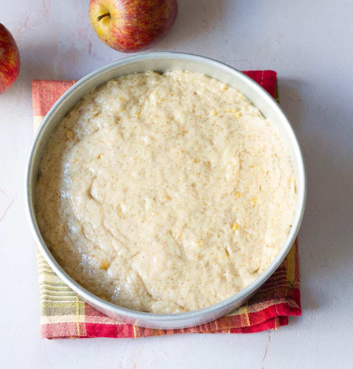 Cake batter on top of the arranged apples in the cake tin.
