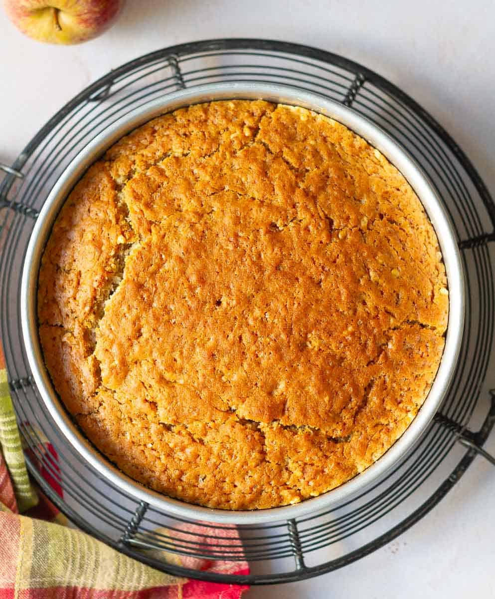 Baked cake in a cake tin on a wire trivet.