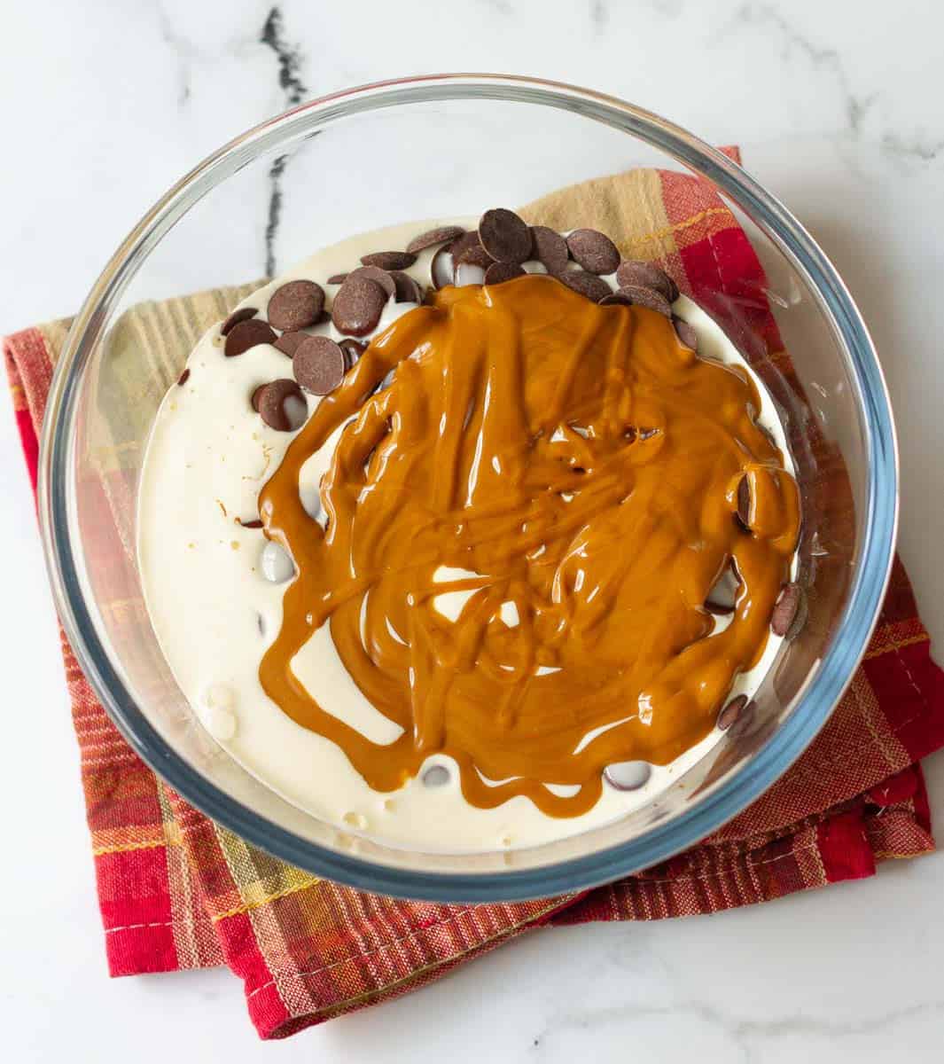 chocolate chips and melted biscoff on top of warm cream in a mixing bowl.