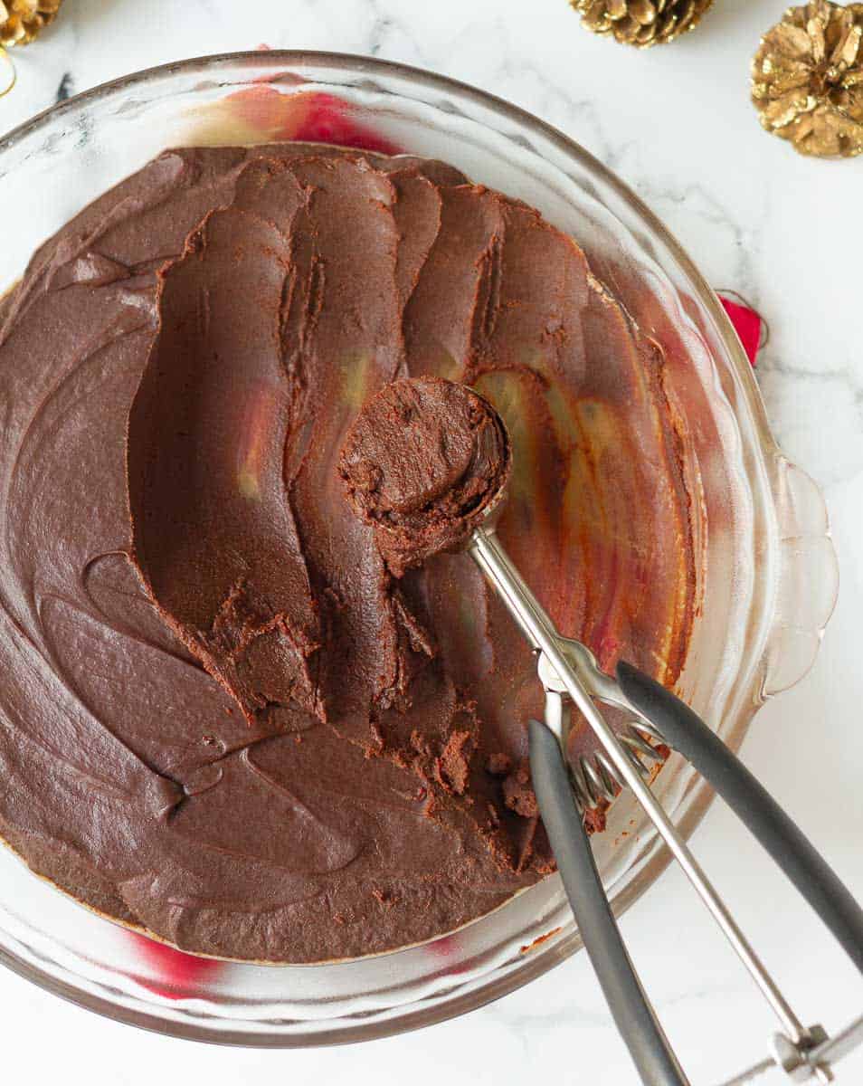 Chocolate truffle mixture in a glass pie dish with an ice cream scoop.