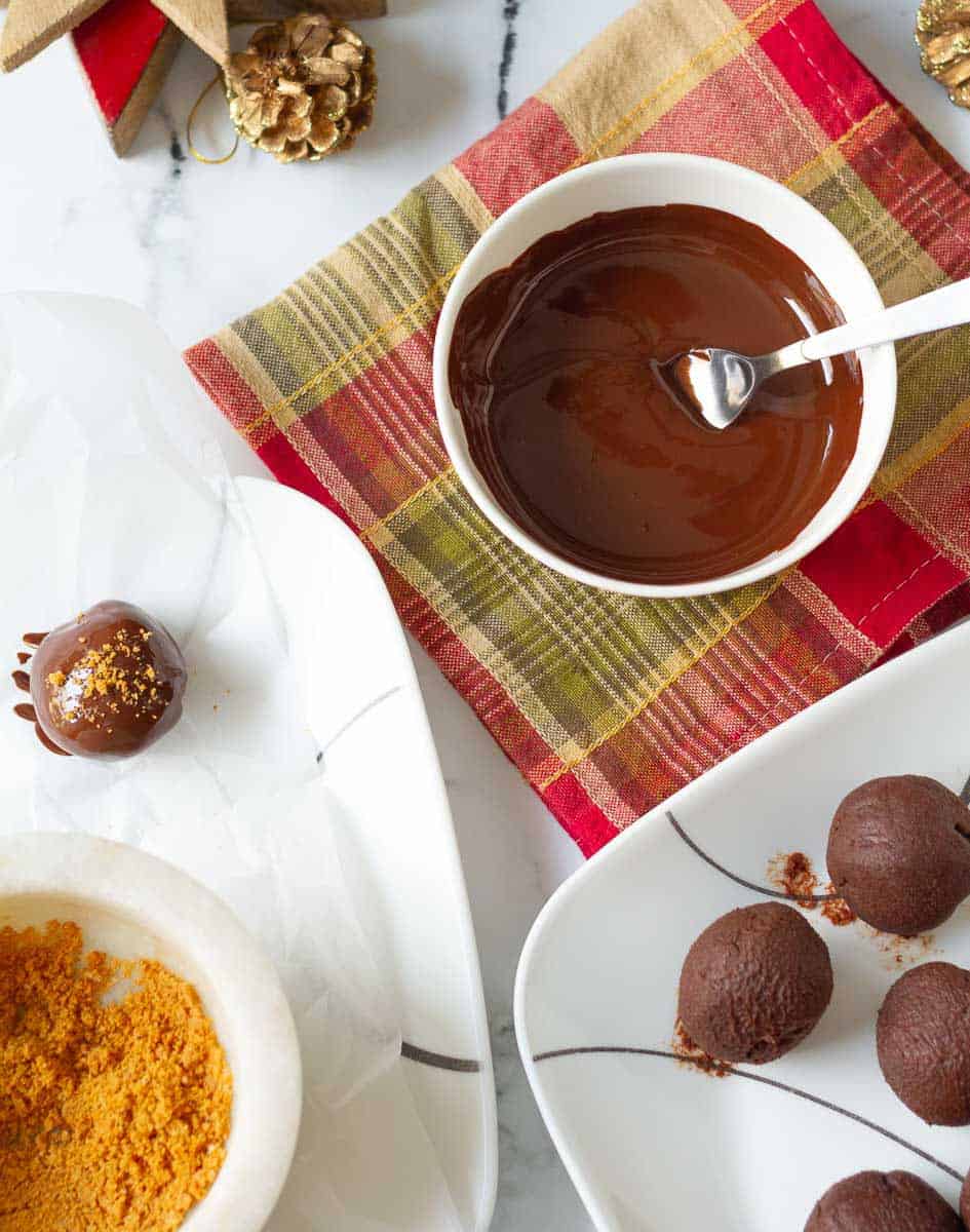 Melted chocolate in a small bowl, truffle balls and one chocolate dipped truffle on a plate.