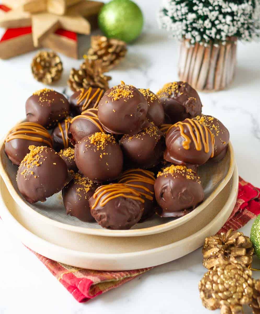 Chocolate dipped truffles decorated with crushed cookies and melted biscoff on a plate.