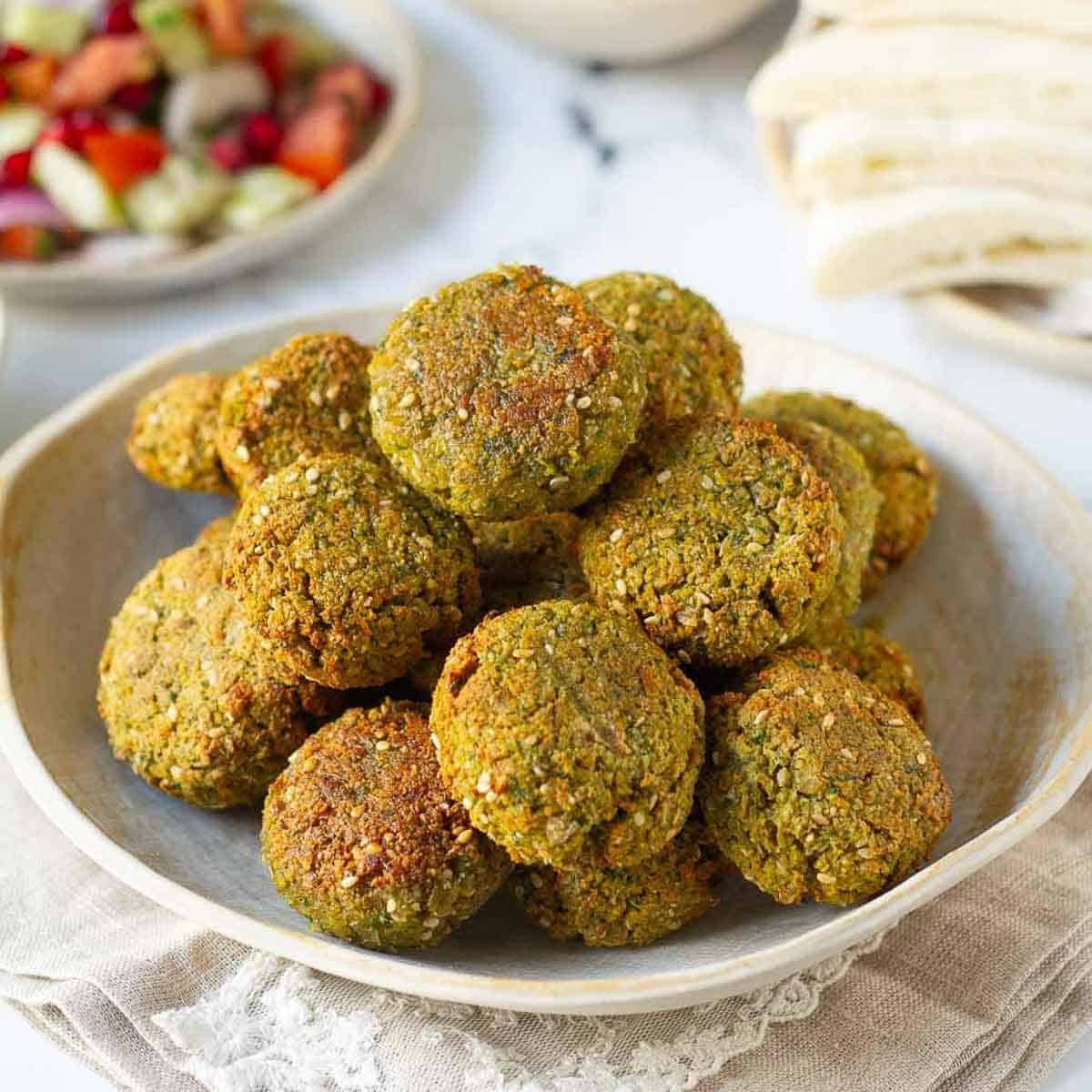 falafels on a plate with a salad and pitas in the background.