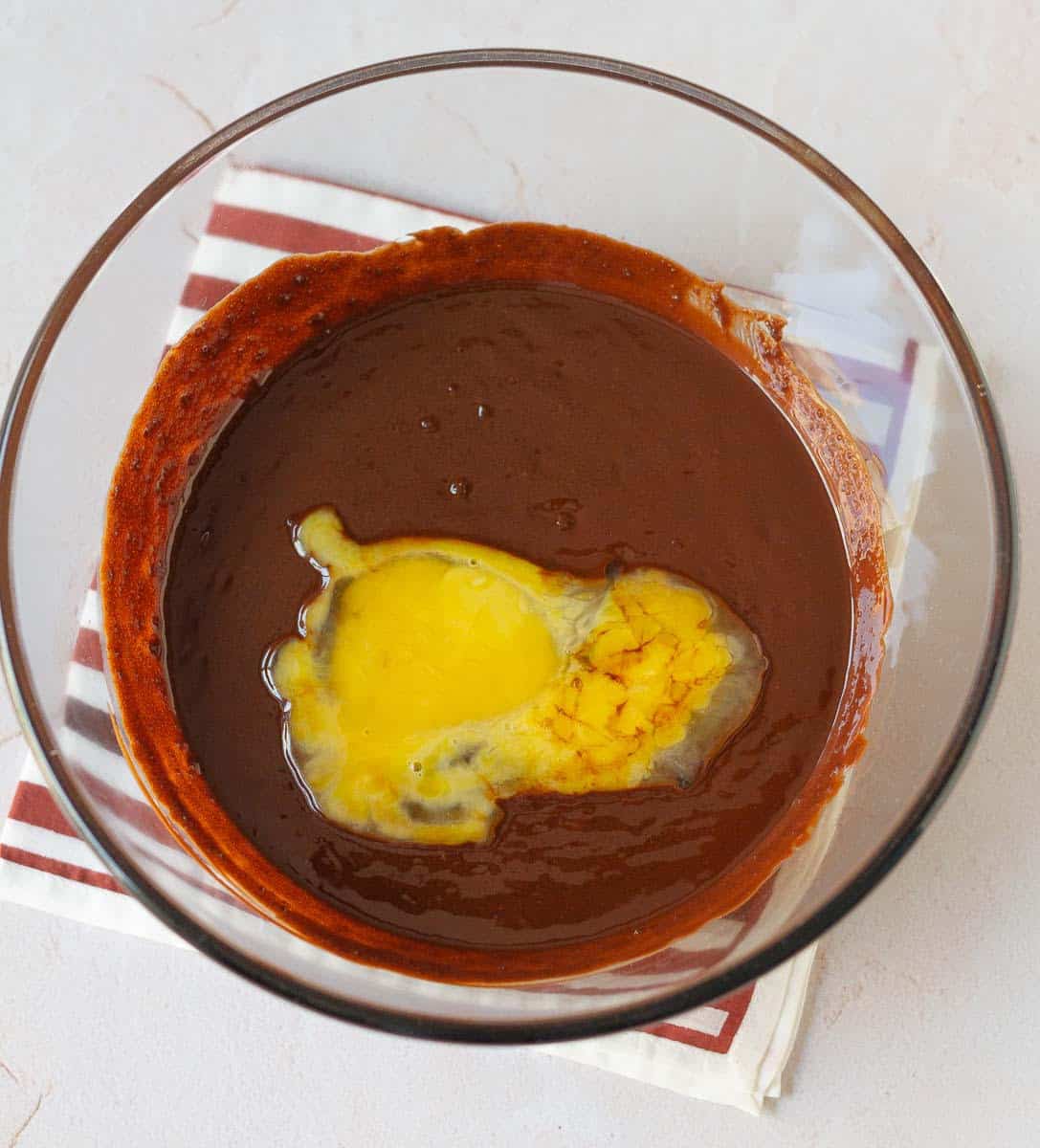 Eggs and vanilla extract on top of chocolate mixture in a bowl.