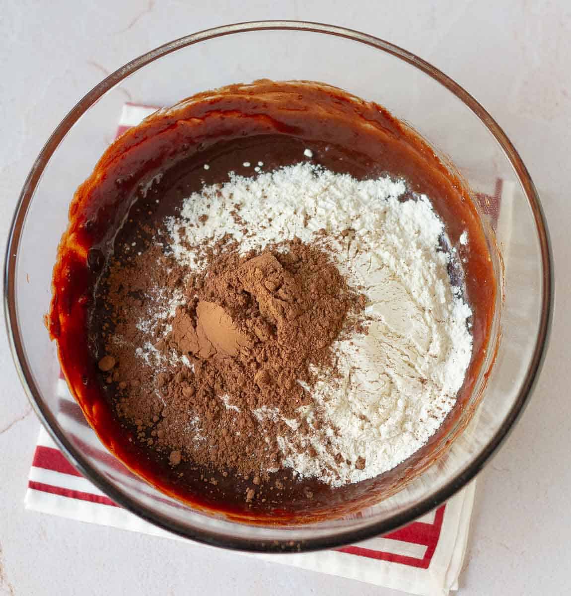 Flour and cocoa powder on top of the chocolate mixture in a bowl.