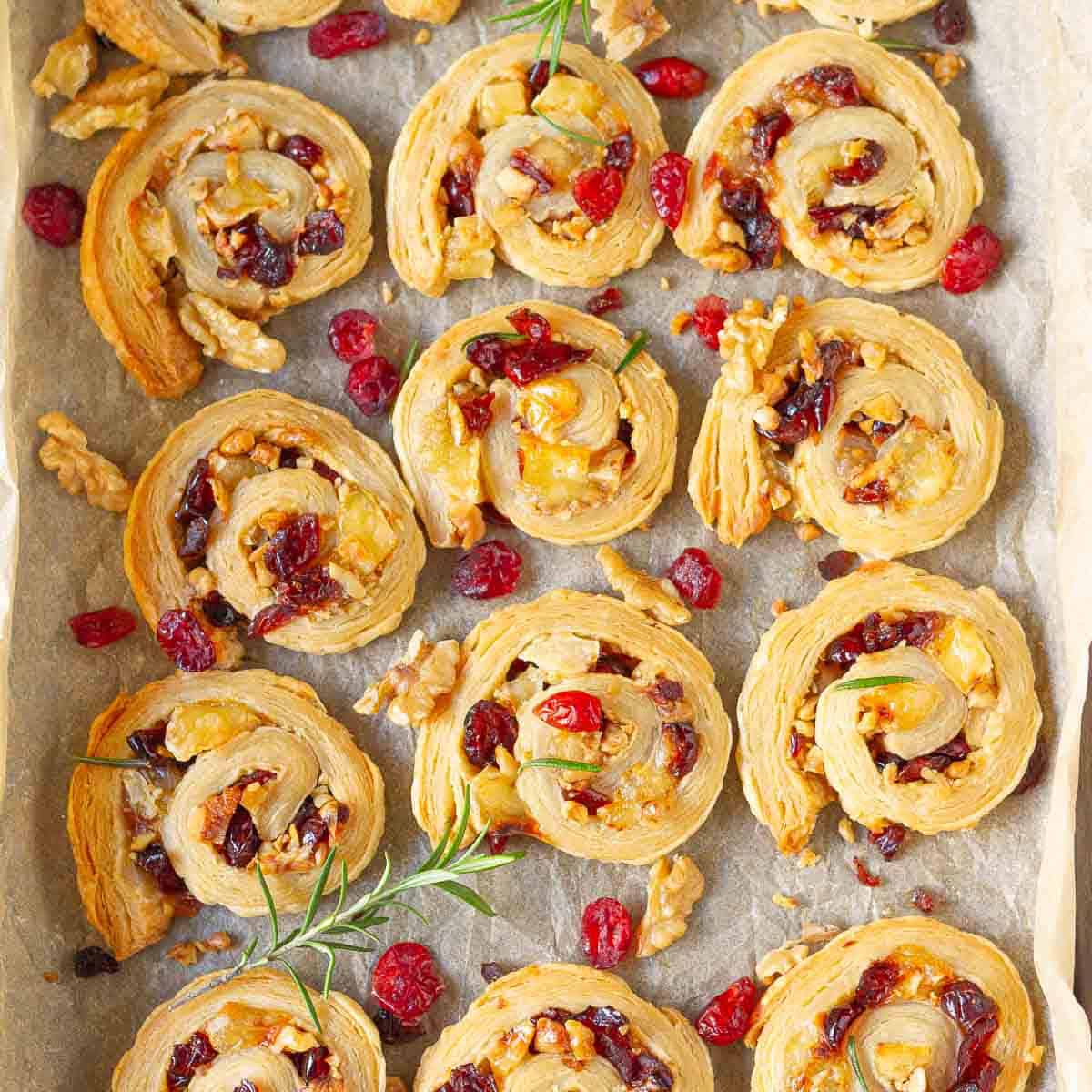 Cranberry Brie Puff Pastry bites on parchment paper with fresh rosemary.