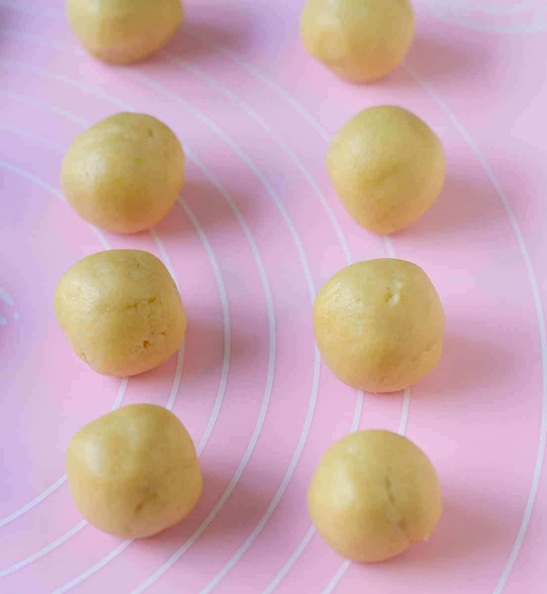 Balls of cookie dough on a pink silicone mat.