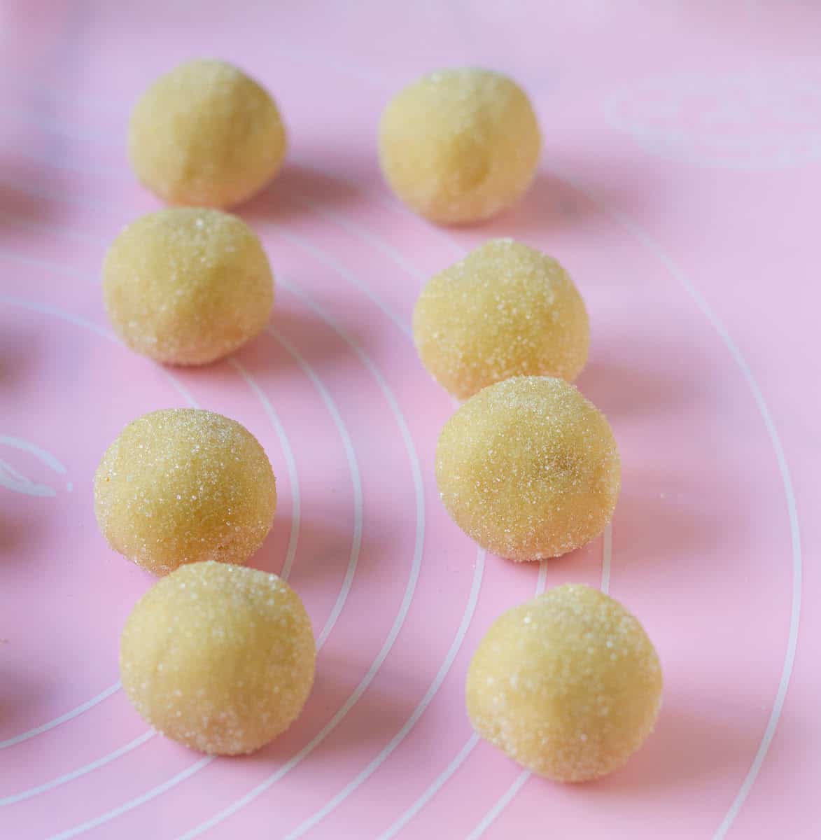 Cookie dough balls rolled in granulated sugar on a pink silicone mat.