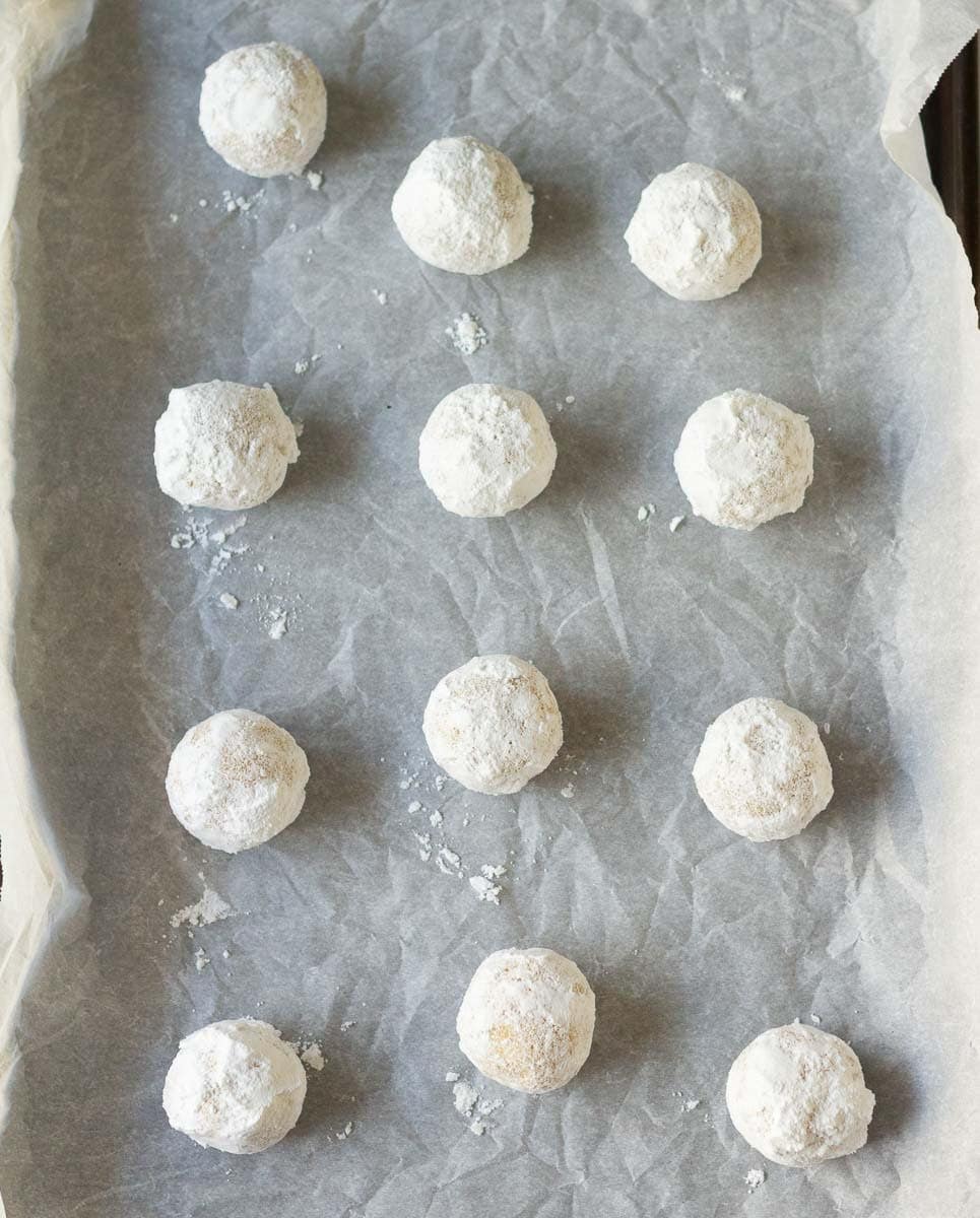 Cookie dough balls rolled in icing sugar on parchment paper.