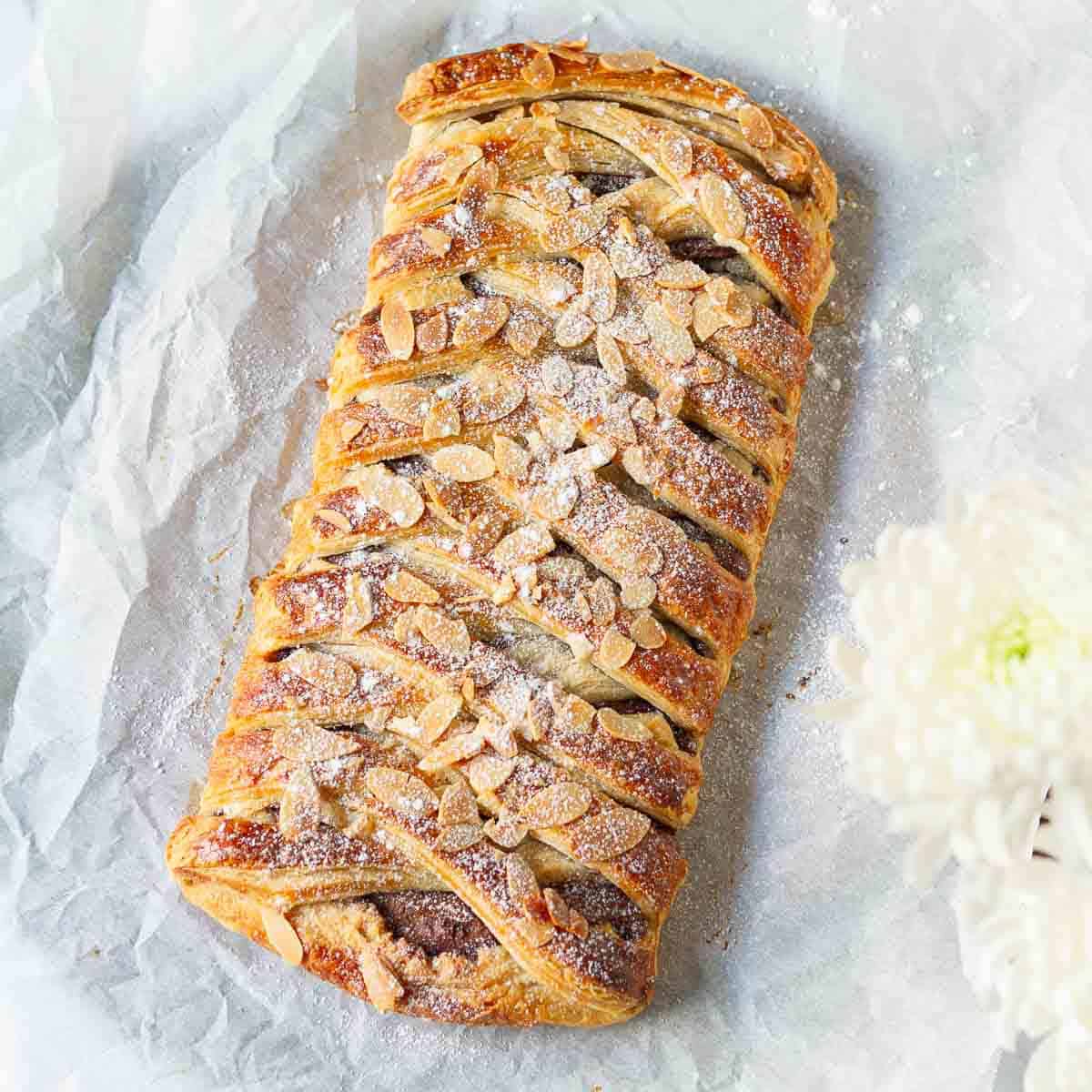 Chocolate puff pastry with almonds on top on parchment paper.