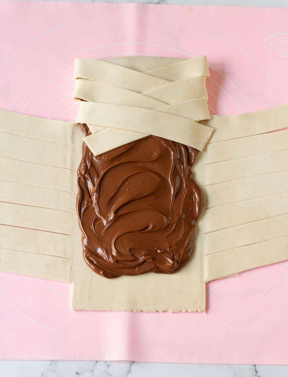 Braiding the pastry strips over the nutella center on a silicone mat.
