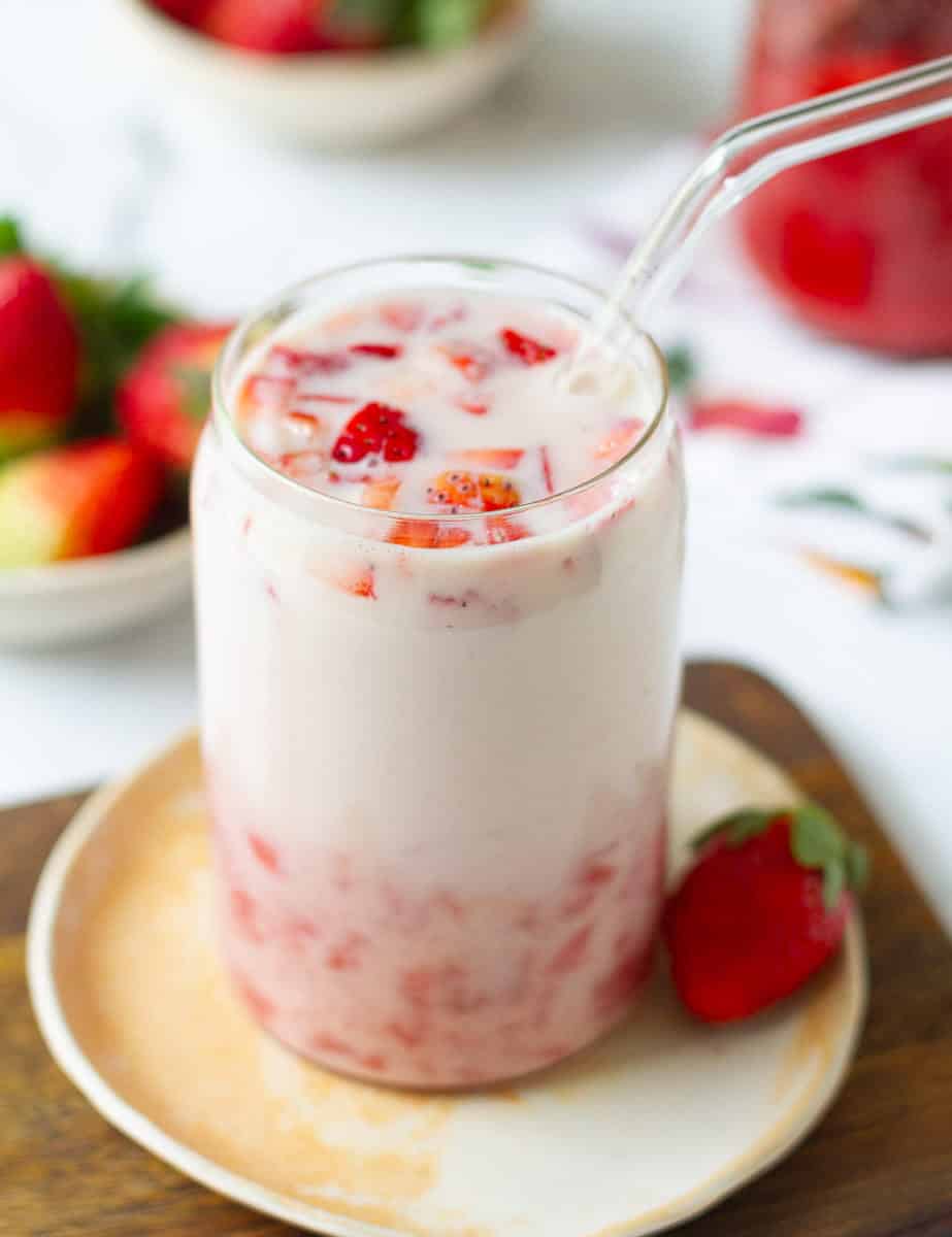 homemade Korean strawberry milk in a glass with a glass straw on a small plate.