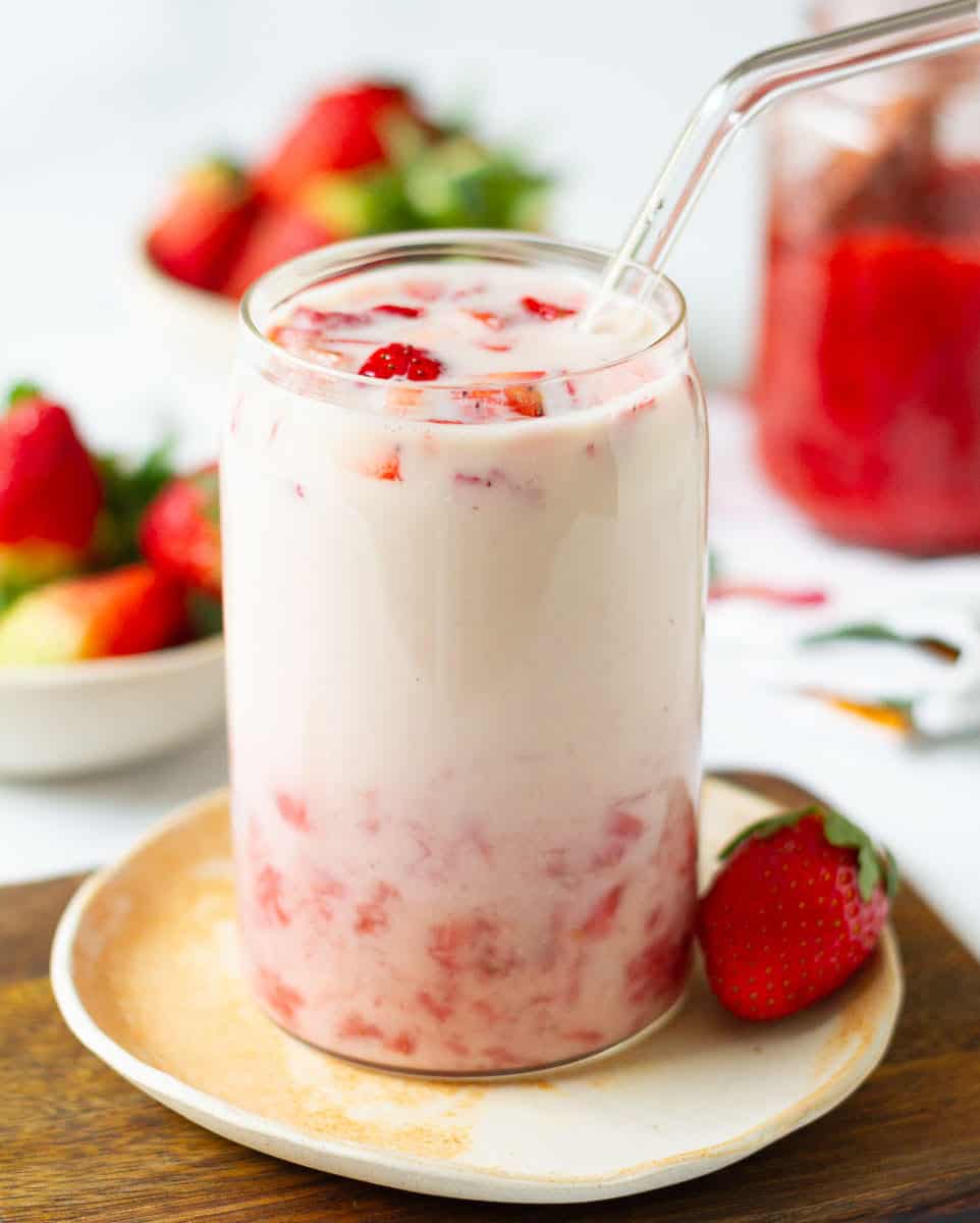 Strawberry Milk in a glass with a glass straw and ingredients in the background.