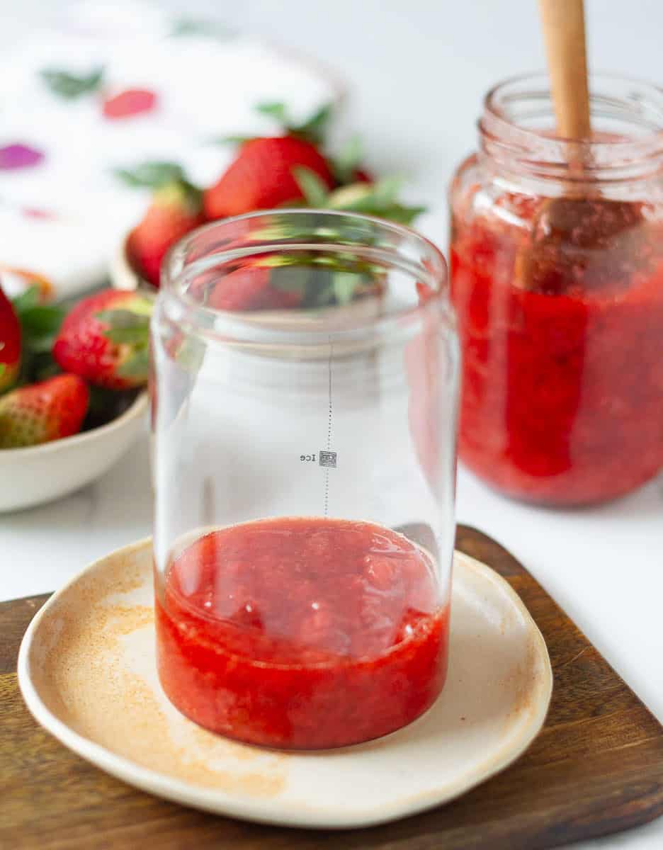 a few spoonfuls of strawberry syrup in glass placed on a small plate.