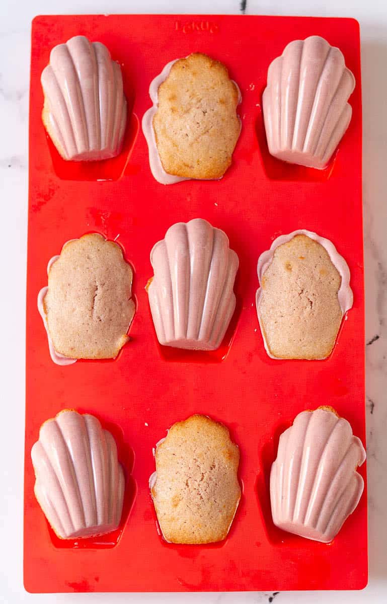 glazing the madelienes with pink hued white chocolate in a red silicone mold.