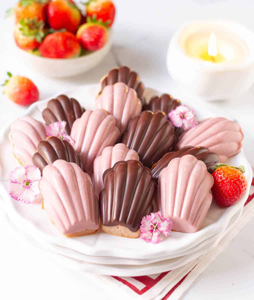 A plateful of madeleines with strawberries and a candle in the background.