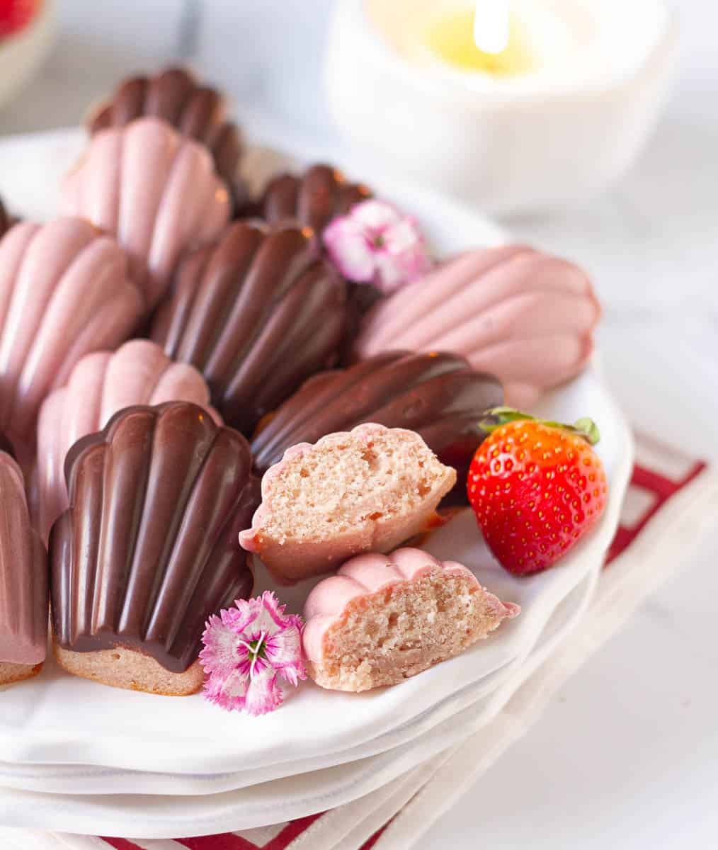 a plateful of madeleines with one madeleine cut into half to show the texture.