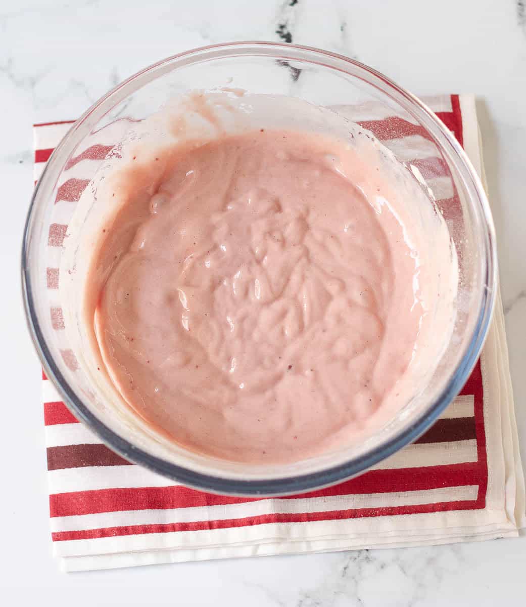 Strawberry syrup, flour, salt and baking powder mixed with eggs in a mixing bowl.