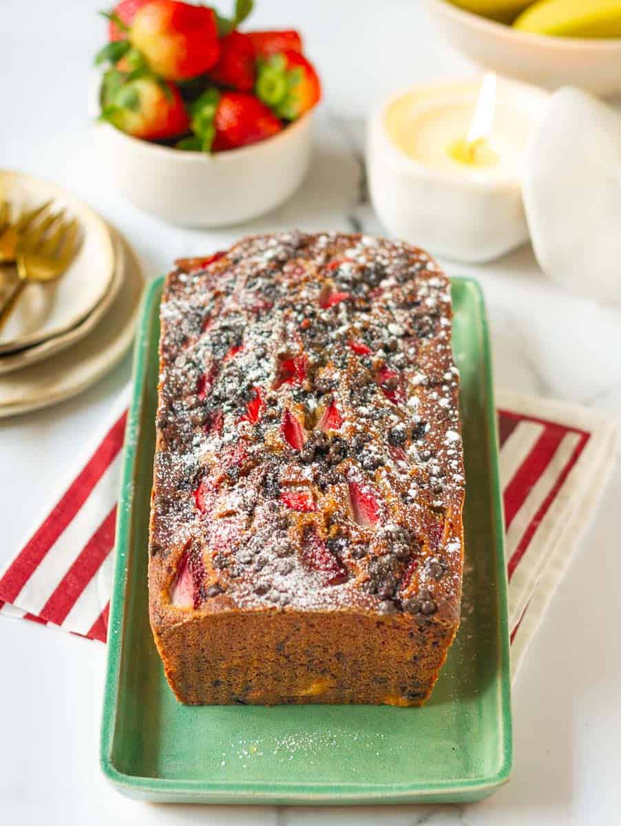Strawberry banana bread on a green serving platter with ingredients in the background.
