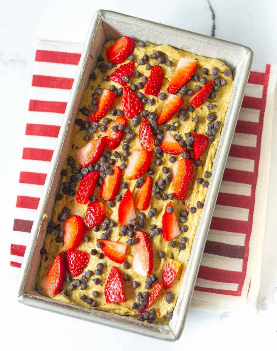 cake batter topped with chopped strawberries and chocolate chips in a loaf tin.