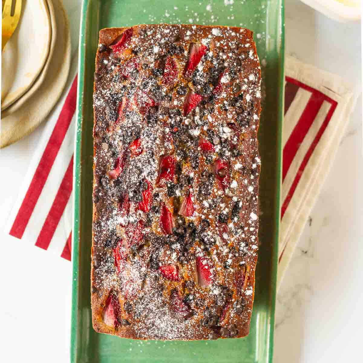 Strawberry banana bread, dusted with powdered sugar, on a green serving platter.