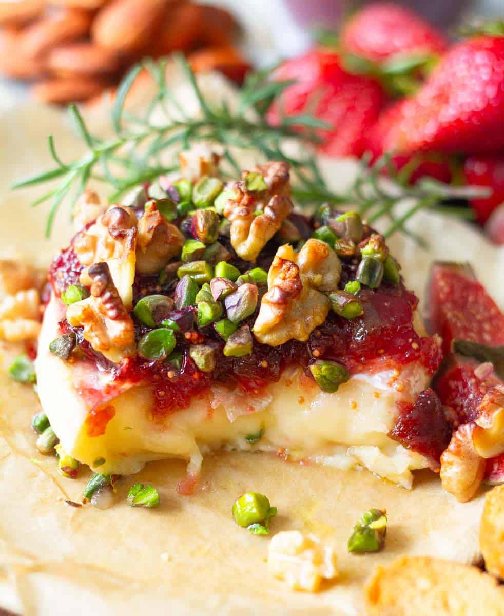 Baked Brie with a piece cut and topped with fig jam, walnuts and pistachios on top.