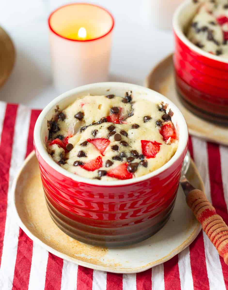 strawberry mug cake in a red ramekin on a small plate with a red spoon.