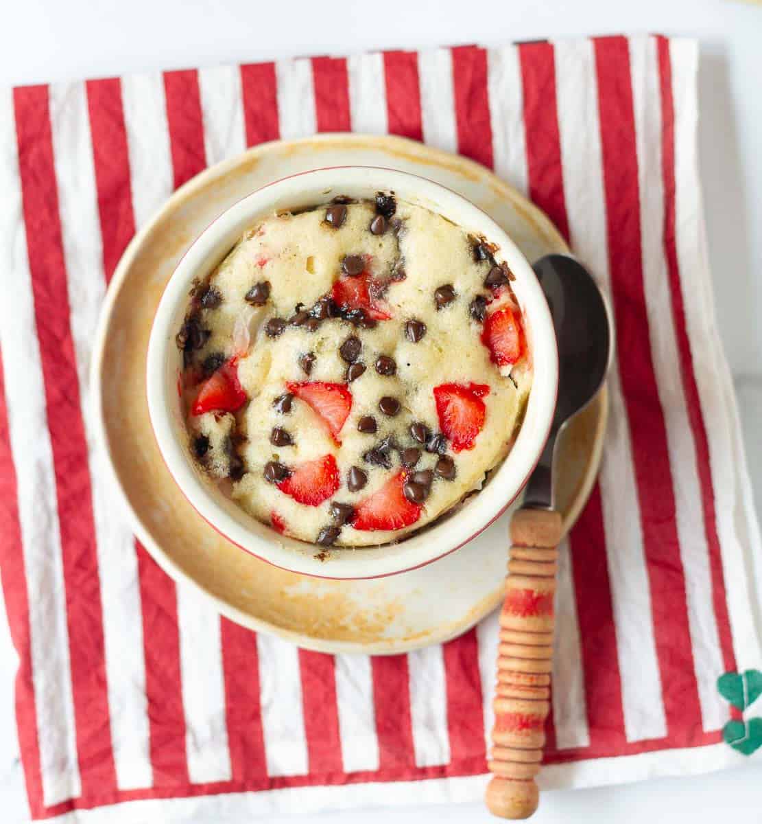 Mug cake baked and ready to eat in a ramekin on a small plate with a spoon.