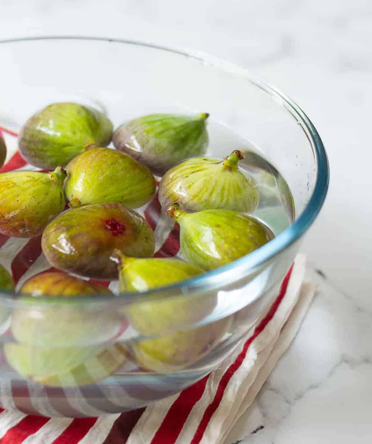 fresh green figs in a glass bowl of water for cleaning.