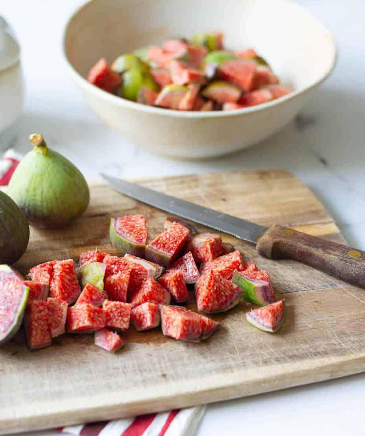 whole and chopped green figs on a wooden chopping board with a knife.