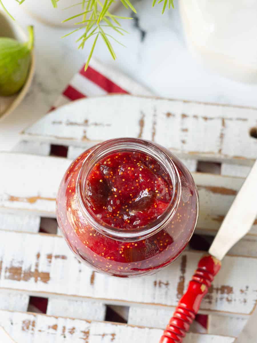 Homemade Fig Jam in a glass jar with a knife on a white wooden trivet.