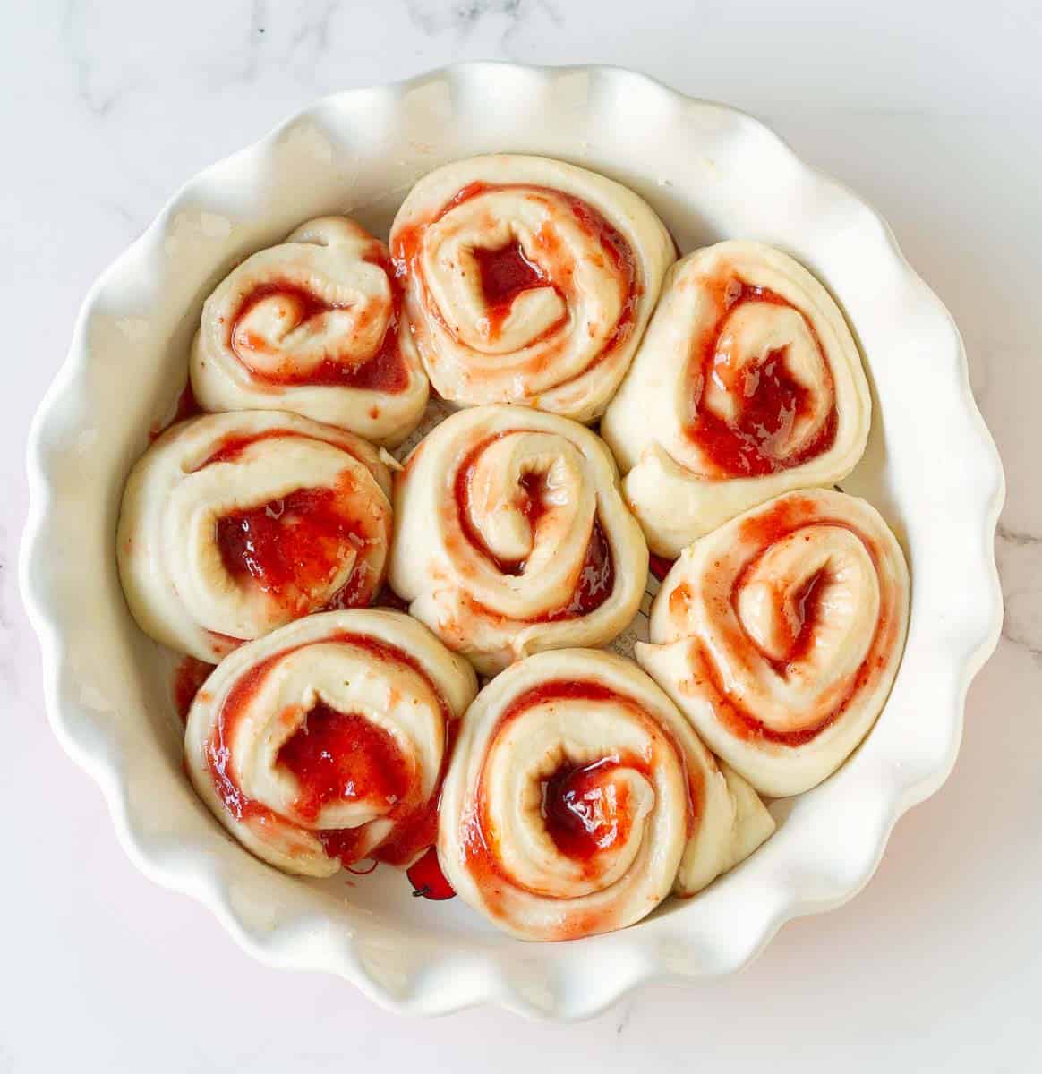 proofed strawberry rolls in a round baking dish.