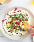 A hand scooping out dip on a crostini from a bowl.