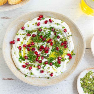 Creamy dip in a bowl garnished with parsley and pomegranate arils.